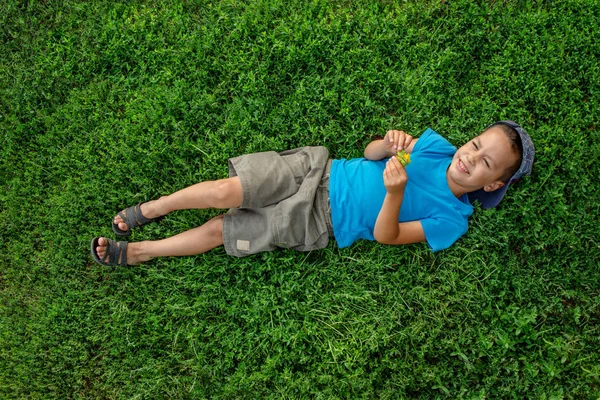 Een jongetje ligt op het groene gras en droomt van iets. — Stockfoto