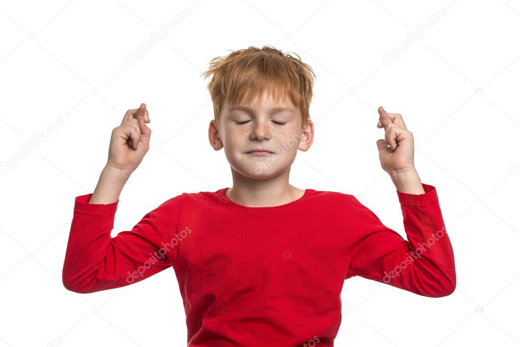 A funny red-haired boy  closing his eyes crossing his fingers on