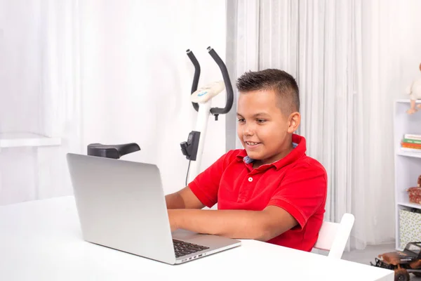 Un escolar está sentado en una mesa con un portátil en la habitación . — Foto de Stock