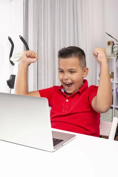 Un escolar está sentado en una mesa con un portátil en la habitación . — Foto de Stock