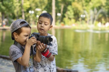 İki çocuk gölün kenarında durur ve doğanın fotoğraflarını çeker.