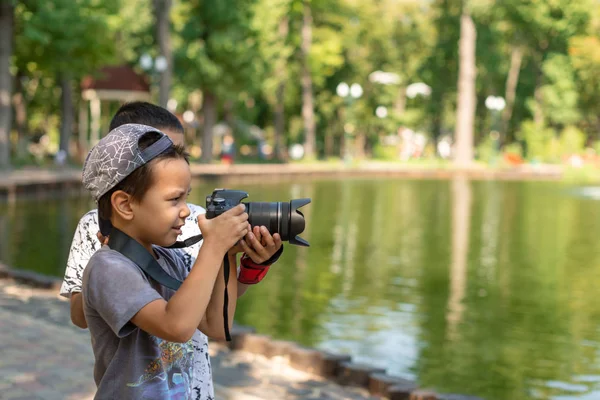İki çocuk gölün kenarında durur ve doğanın fotoğraflarını çeker.