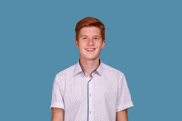 Tiro de um adolescente sorridente com cabelo vermelho contra as costas azuis — Fotografia de Stock