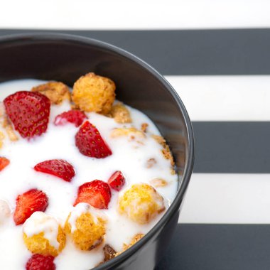 Siyah ve beyaz çizgili bir standın üzerinde siyah bir fincanda çilekli çıtır çıtır. Sağlıklı yaşam biçimi, sağlıklı yemek..