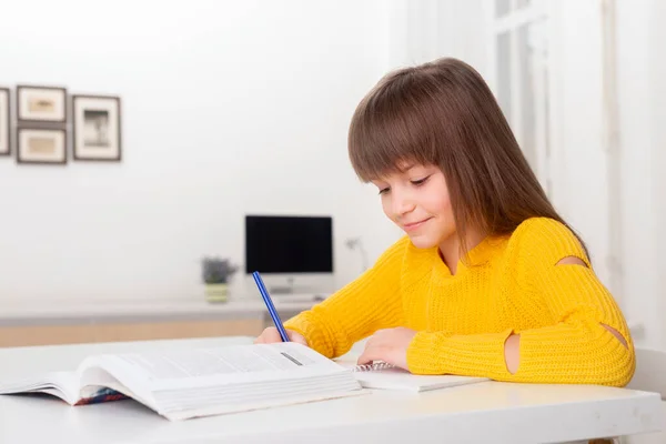 Shot of  schoolgirl with long hair and bangs sitting at a table at home  and doing homework. Back to school