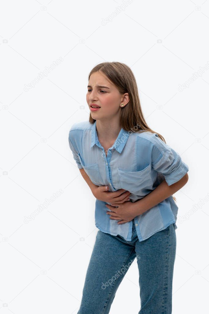 Emotional waist up portrait of a young girl wearing  blue blouse and jeans against white background.  Her stomach hurts
