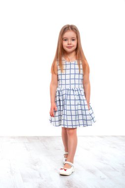 Uzun sarı saçlı, gülümseyen küçük bir kızın tam boy portresi stüdyoda beyaz arka planda.