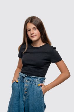 Yarım boy gülümseyen genç kız portresi. Uzun sarı saçlı, siyah gömlekli ve elleri cepli genç kız. Stüdyoda beyaz arka planda.