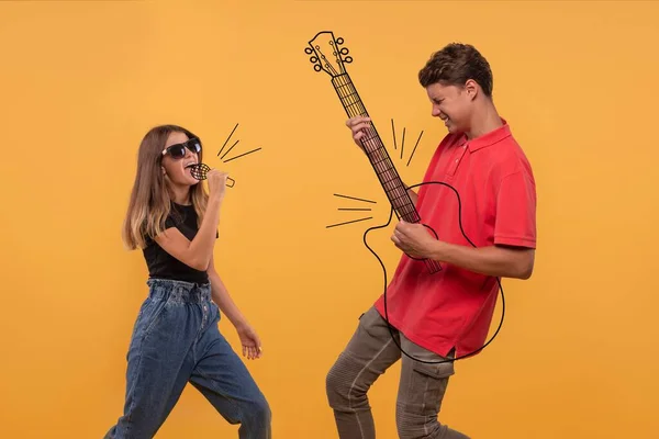 Genç bir kız hayali bir mikrofona şarkı söylüyor. Bir adam duygusal olarak hayali bir gitarı stüdyoda sarı arka planda çalıyor.
