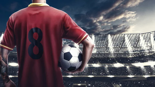 Футболіст стоїть з м'ячем на переповненому стадіоні на фоні Ліцензійні Стокові Зображення