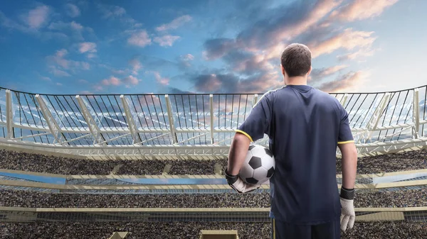 Футболист, стоящий с мячом на фоне переполненного стадиона — стоковое фото