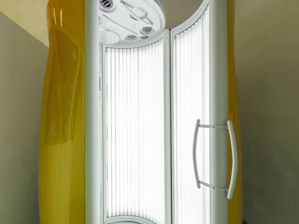 Вертикальный солярий с светящимися желтыми ультрафиолетовыми лампами для загара и ухода за кожей — стоковое фото