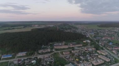 Kamera yaz akşamı köyünün üzerinde uçuyor. Köy ormanının ortasında. Ormanda mobil iletişim kulesi var. Hava görüntüsü. Rusya, Sverdlovsk bölgesi, Sysert bölgesi, Oktyabrskiy köyü
