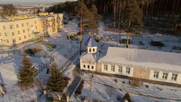 村の教会の空中ビュー 教会の隣に幼稚園があります 教会の森の後ろ 外は雪が降っている ロシア スヴェルドロフスク地方 オクタイブラスキー州 — ストック動画