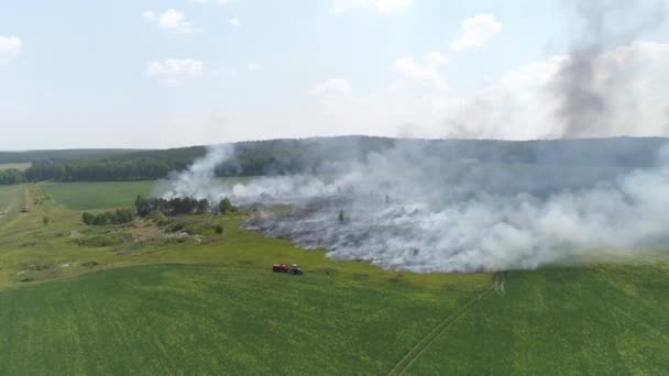 Vue aérienne du feu sur le terrain. Brûler l'herbe et les ordures. A côté d'un tracteur avec un baril d'eau, va éteindre le feu. Près de la forêt. Journée ensoleillée d'été