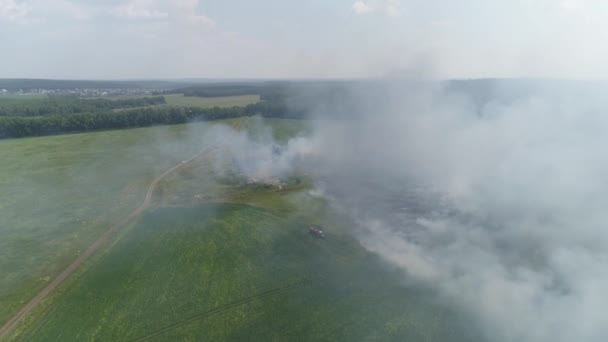 Vue aérienne du feu sur le terrain. Brûler l'herbe et les ordures. A côté d'un tracteur avec un baril d'eau, un homme éteint un feu. Près de la forêt. Journée ensoleillée d'été