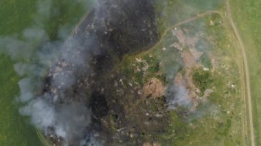 Alanda havadan ateş görünüyor. Çimenleri ve çöpleri yakmak. Kamera geri dönüyor ve köyün panoramik görüntüsünü veriyor. Ormanın yakınında. Yaz güneşli bir gün