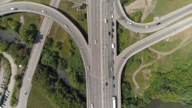 Otobanın yukarıdan aşağıya bakan manzarası. Şehirdeki araba trafiğiyle kavşak. Yeşil ağaçların ve çimlerin ortasındaki otoban. Yaz güneşli bir gün