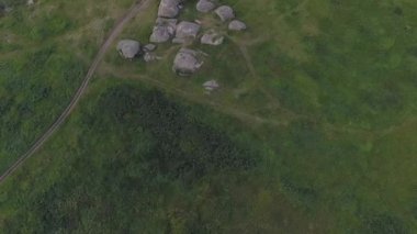 Göl kenarındaki bir tarladaki devasa taşların (kayaların) havadan görünüşü. Yakınlarda toprak bir yol var. Mavi gökyüzündeki bulutlar. Yaz güneşli bir gün