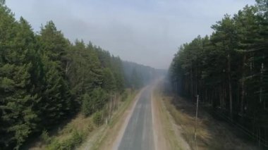 Orman yolunda hava manzarası ve orman yangınından çıkan duman. Arabalar yol boyunca gider. Yangının yanında bir itfaiye arabası var. Yaz, sıcak güneşli gün.