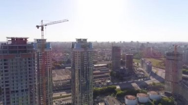 Şehirdeki çok katlı binaların hava manzarası. Bazı evler inşa edildi, bazı evler hala yapım aşamasında. Çatılarda helikopter pistleri de var. İnsanlar çatılardan birinde yürüyorlar. Kamera evlerin etrafında uçuyor.