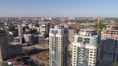 Şehirdeki çok katlı binaların hava manzarası. Bazı evler inşa edildi, bazı evler hala yapım aşamasında. Çatılarda helikopter pistleri de var. Kameralar evlerden uçup gidiyor.