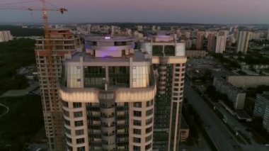 Akşam şehrindeki gökdelenlerin hava görüntülerine göre gün batımında önemli bir yerleşim bölgesinde. Arka planda modern şehir. Çatıdaki insanlar ve parti. Bazı evler inşa edildi, bir ev hala yapım aşamasında.