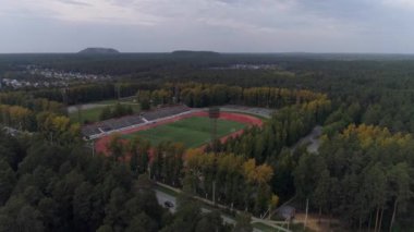Sarı-yeşil ormanların yanındaki futbol stadyumunun havadan görünüşü. İnsanlar stadyumda futbol oynuyor ve spor yapıyorlar. Rusya, En İyi Şehir