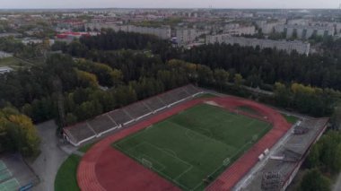 Futbol stadyumunun havadan görünüşü. Küçük kasabadaki sekiz sıkıcı apartman ve sarı-yeşil orman. İnsanlar stadyumda futbol oynuyor ve spor yapıyorlar. Rusya, En İyi Şehir