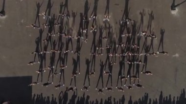 Asfalt alanda dans eden bir grup gencin yukarıdan aşağı hava görüntüsü. Gölge dansı. Yakınlarda bir seyirci topluluğu var. Hızlı kalabalık. 