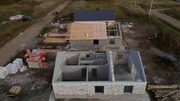 Aerial view of construction site. You can see how houses is being builds. Drone is flying above area where are almost finished house, house without roof, house walls. Near the construction site a forest — Stock Footage Aerial View Construction Site You Can See How Houses Being Stock Footage