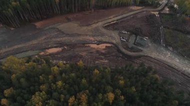 Büyük şehrin yakınındaki hava manzaralı yol inşaatı. Ormanda bir yol inşa etmek için inşaat makineleri. Yeni otoyol için geniş, düz bir orman şeridi olan kuş gözüyle ormanların yok olması.