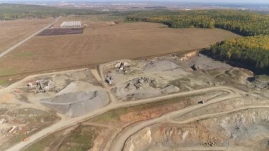 Taşıyıcılar ve ezicilerle endüstriyel alanın havadan görüntüsü. Moloz yığınları arasında. Bölgeye kamyonlar geliyor. Ormana ve yola yakın. Sonbahar güneşli bir gün