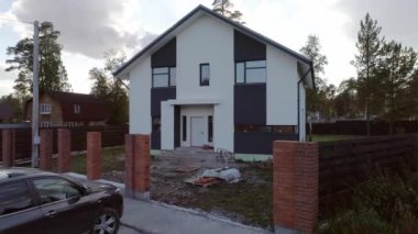 Güzel bir semtteki yeni, modern bir ev kulübesinin havadan görünüşü. Yumuşak fayanslardan yapılmış çatı. Evin etrafına bir çit inşa ediliyor. Ağaçlar ve çimenler toprakta yetişir.