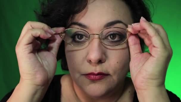Mature latina woman puts on glasses with green background — Stock Video