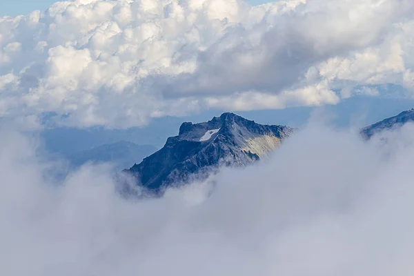 Pico escarpado de uma montanha saindo de nuvens e nevoeiro — Fotografia de Stock