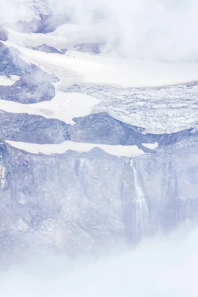 Waterfall from glacial melt tumbled down long drop hidden by fog — Stock Photo, Image