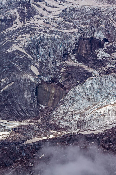 vertical shot of glaciers and harsh mountain side at high altitude with fog