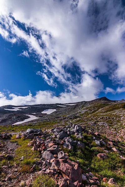 White fluffy clouds in a bright blue sky over a mountain landscape — Stock Photo, Image