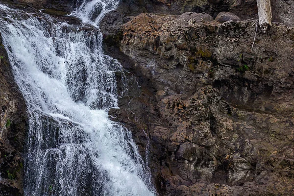 Kleiner weißer Wasserfall stürzt über dunkle Felswand — Stockfoto