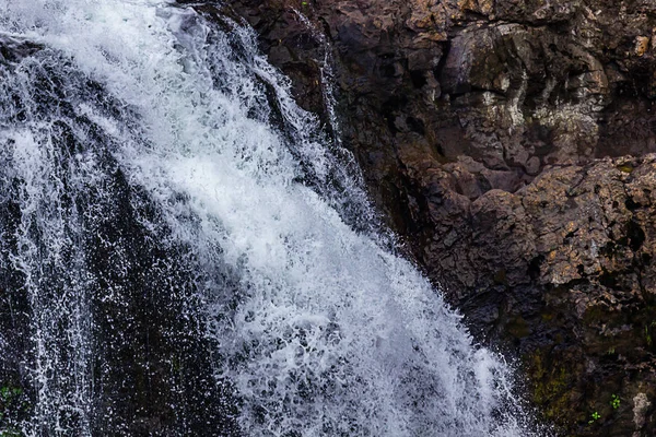 Weißer Wasserfall gefroren, als er von dunklen Steinen herabstürzt — Stockfoto