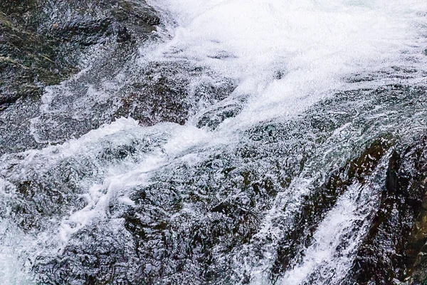 Helder wit water textuur contrasteert donkere zomer stenen — Stockfoto