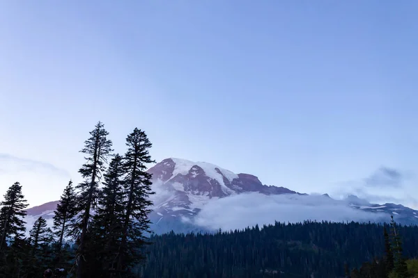 Montaña cubierta de nieve contra árboles del bosque oscuro y nubes blancas brillantes — Foto de Stock