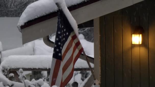 Σπίτι σε χιόνι με αμερικάνικη σημαία που πετάει στο χιόνι που πέφτει — Αρχείο Βίντεο