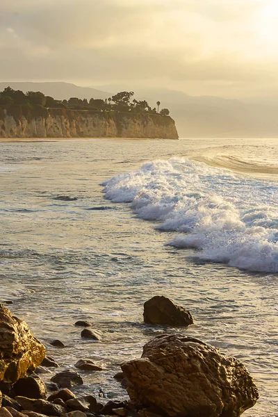 Vague moussante se brisant au lever du soleil avec rivage rocheux — Photo