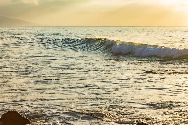 Onda de ondulação formando com espuma quebrando contra a extensão do oceano com céu amarelo — Fotografia de Stock