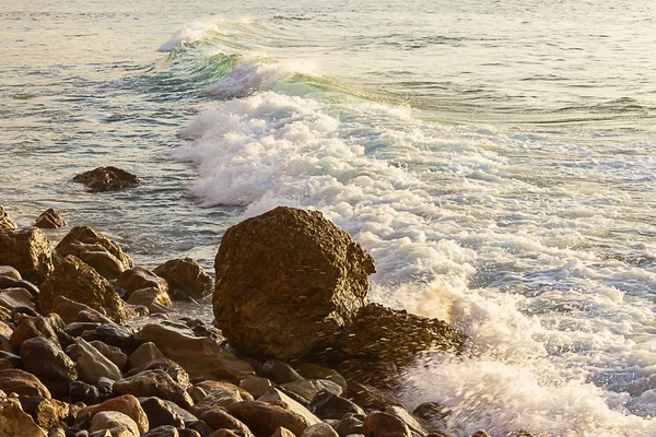 Onda di rottura schiumosa con backsplash e schiuma contro massi sulla riva rocciosa con onda che diminuisce nell'oceano — Foto Stock