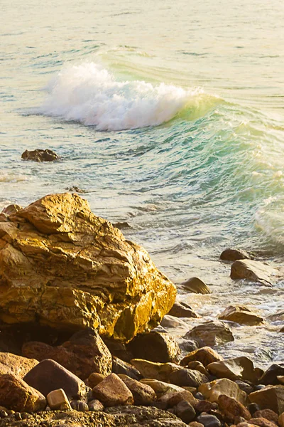Pastel gekleurde brekende golf op rotsachtige kust — Stockfoto