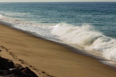 kumlu plajda dalga kırma, backwash, ayak izleri ve kayalar ile