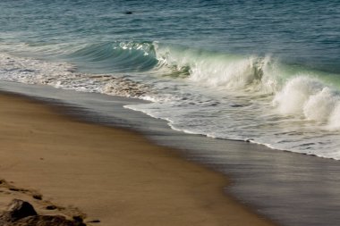 kumlu plajda dalga kırma, backwash, ayak izleri ve kayalar ile